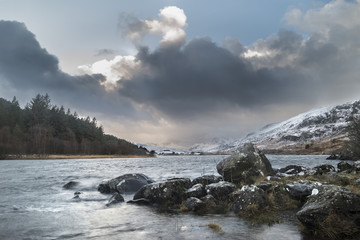 Beautiful Winter landscape image of Llynnau Mymbyr in Snowdonia National Park with snow capped mountains in background
