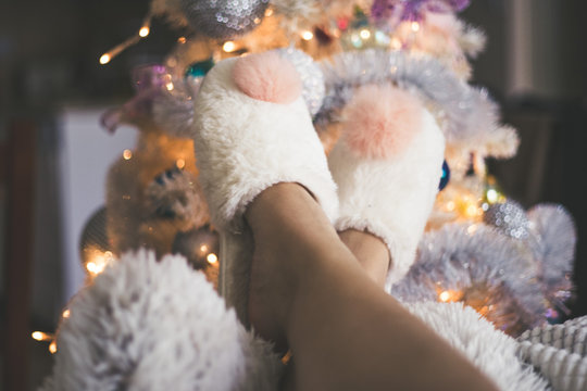 Woman legs in slipper front of a christmas tree.