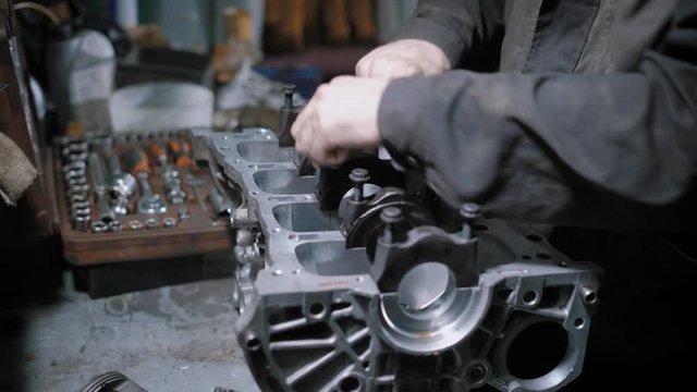 worker is disassembling car engine in a repair shop, twisting bolts and detaching details with force