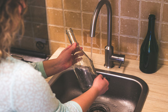 Woman dishwash a glass bottle with water from the faucet in the kitchen a close up view on the running water.