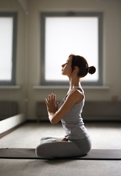 Relaxed young sportswoman doing yoga and meditating in studio