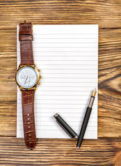 Pen and wrist watch on blank notepad. Top view.