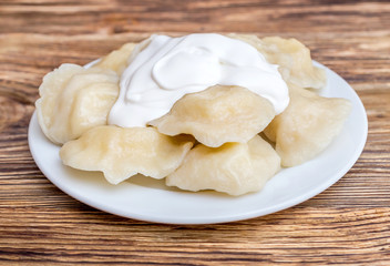 Plate with boiled varenyky and sour cream on wooden table.