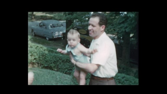 1953 Glamorous mom and dad toss baby boy with antique cars