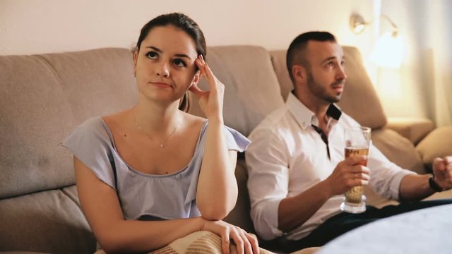 Woman is sading when her husband is watching TV at home.
