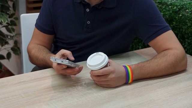 a young man with a rainbow symbolism in a cafe, uses a telephone