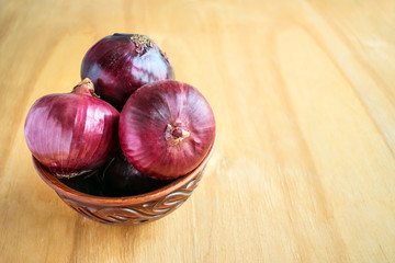 Three whole red onion bulbs in brown rustic bowl on wooden background. Red onions, are cultivars of the onion (Allium cepa) with purplish red skin and white flesh tinged with red.