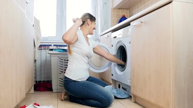 Slow motion video of happy laughing woman taking clothes out of washing machine and throwing in air