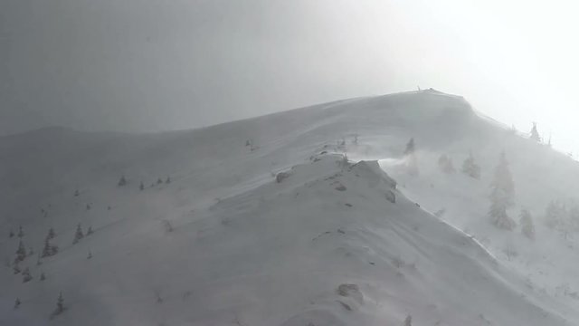 High speed winds drift snow from mountain ridge during a storm blizzard in winter