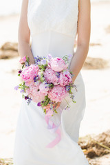 Bride on the beach. Woman with wedding bouquet of peony flowers.