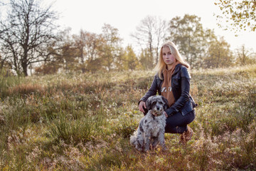 Naklejka na ściany i meble Girl with her dog sitting on a meadow in early morning sunlight