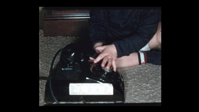 1953 Baby boy plays with vintage antique rotary telephone