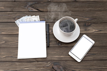 notebook, dollar bills, smartphone, cup of coffee on a wooden background