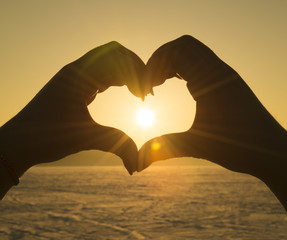 Young woman making a heart shape with her fingers on the beach. against the sunset
