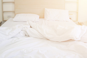 Comfortable bedroom unmade white bedsheet messy and pillow after sleep with sun light in the morning effect