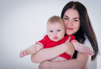 Young happy mother with baby boy shooting in the photo studio, smiling, posing on white background