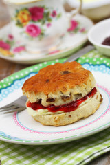 Delicious traditional English scone with fresh clotted cream and strawberry jam, closeup
