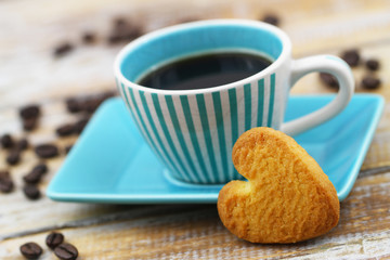Heart shaped crunchy cookie leaning against cup of coffee on rustic wooden surface
