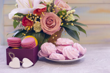 Obraz na płótnie Canvas Romantic festive compositions with flower basket and sweets- a plate of marshmellows and a box of macaroons agains a light colored wooden background.St. Valentines, anniversary, wedding concept