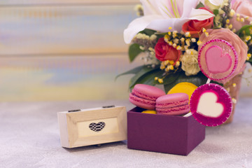 Romantic festive compositions with flower basket, a box of macaroons, lolipop with hearts and a wooden casket with a gift. Light colored wooden background.St. Valentines, anniversary, wedding concept