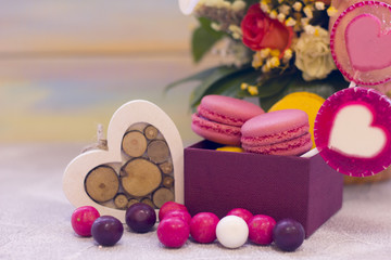 Romantic festive compositions with flower basket, a box of macaroons, lolipop with hearts and a wooden heart. Light colored wooden background.St. Valentines, anniversary, wedding concept