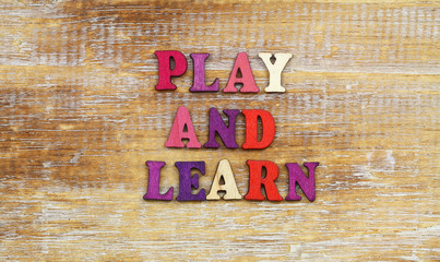 Play and learn sign written with colorful wooden letters on rustic surface
