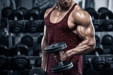 Naklejka na ściany i meble Muscular man working out in gym doing exercises with dumbbells, bodybuilder