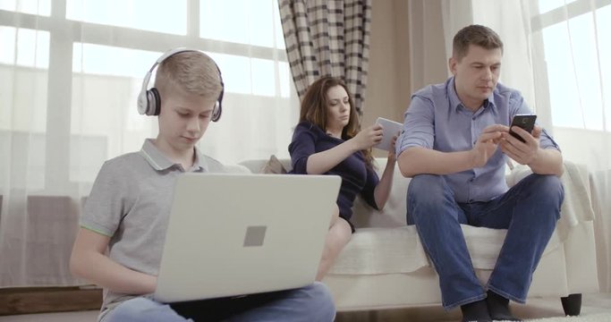 Family of three people uses gadgets and does not communicate. Сoncept of Internet addiction people. Dolly shot 4K