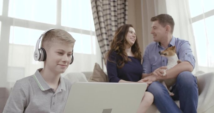 Happy parents enjoy watching their son using a laptop. Dolly shot. 4K