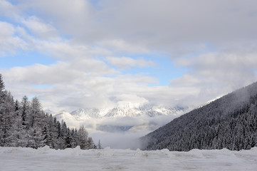 Obraz premium Panorama of Austrian Stubai Alps with mountain ranges and trees covered in snow and blue sky and clouds in winter