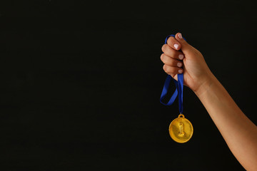 Plakat Woman hand holding gold medal against black background. Award and victory concept.