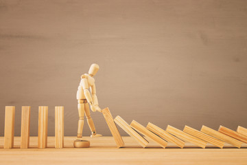 A wooden dummy stopping the domino effect. retro style image executive and risk control concept.
