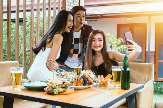Two Asian women and one men hand holding mobile phone Taking pictures with  food on table