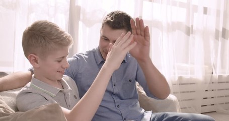 Young handsome man and his son teen sitting on the couch with a tablet 4K - Powered by Adobe