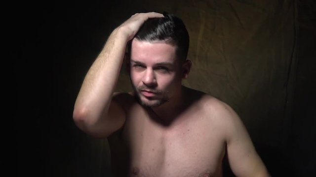 A man stands topless and straightens his hair.