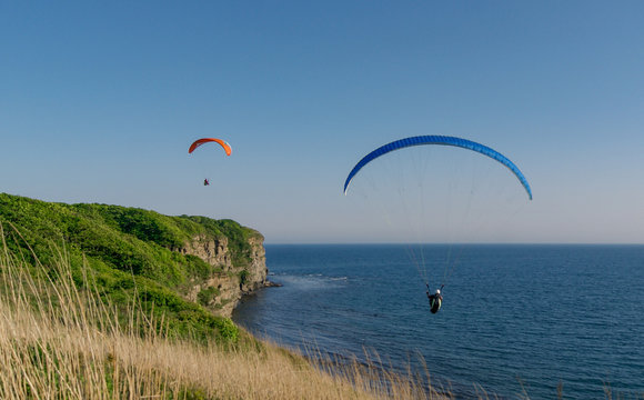 Two persons flies on paraplane above cliff break
