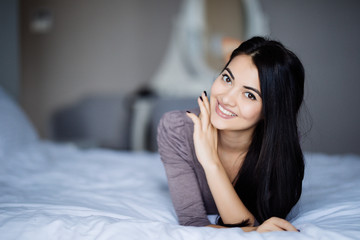 Young woman looking at camera and smiling while lying on the bed at home