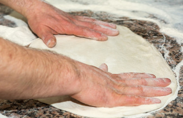 Fototapeta premium the chef's hands knead the dough to make pizza in the kitchen. Food, italian cuisine and cooking concept.Food, italian cuisine and cooking concept. Preparation of the Italian Pizza