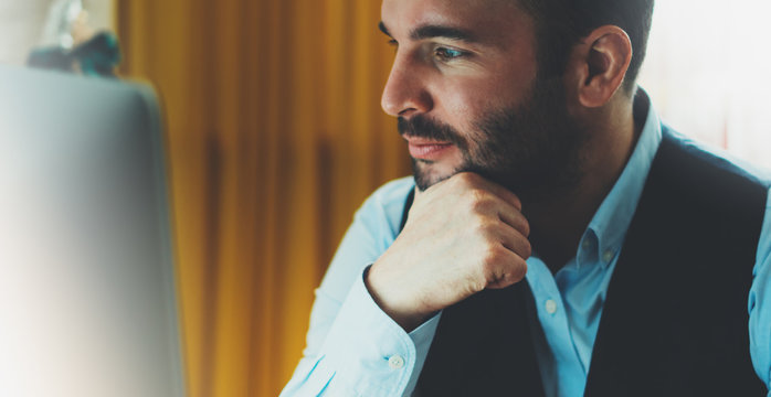 Bearded young businessman working on modern office at night. Consultant man thinking looking in monitor computer. Manager typing on keyboard in coworking workplace, startup project concept in studio