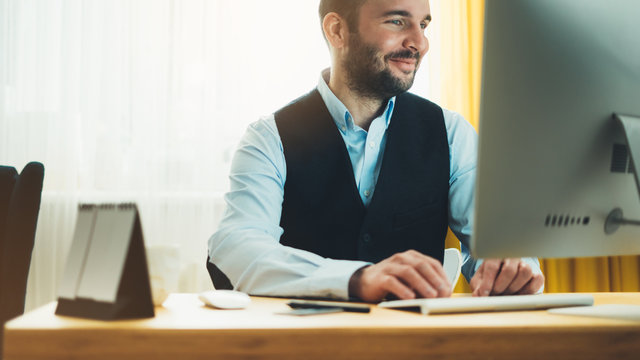 Bearded young businessman working on modern office at night. Consultant man thinking looking in monitor computer. Manager typing on keyboard in coworking workplace, startup project concept in studio