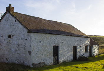 Fototapeta na wymiar An old whitewashed stone built Irish Cottage with a small annex roofed with bangor Blue roofing tiles and rusting corrugated tin sheets