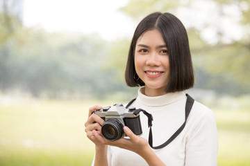 Attractive Asian shot hair woman holding retro camera with smiling, Woman using camera at outdoor place.