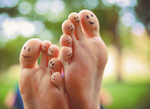 smiley faces on a pair of feet on all ten toes in a park on a hot summer day