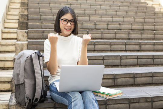 Portrait of Attractive Asian Student Woman sitting at outdoor place. Woman using laptop with Attractive Smiling to Camera. People with Education Concept.