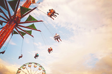 people riding rides and enjoying the summer atmosphere at a state fair at dusk toned with a retro...