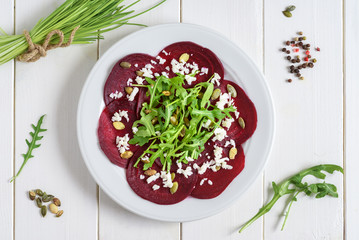 Beetroot carpaccio with rucola leaves and pumpkin seeds on wooden white background.