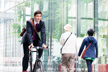 Cheerful young employee with a healthy lifestyle riding an utility bicycle to a modern workplace in...