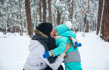 Fototapeta na wymiar Young mother kisses her baby in the winter park