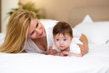 Adorable baby girl in white sunny bedroom have a tummy time. Newborn child relaxing on a bed with her mother