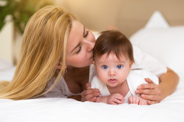 Adorable baby girl in white sunny bedroom have a tummy time. Newborn child relaxing on a bed with her mother